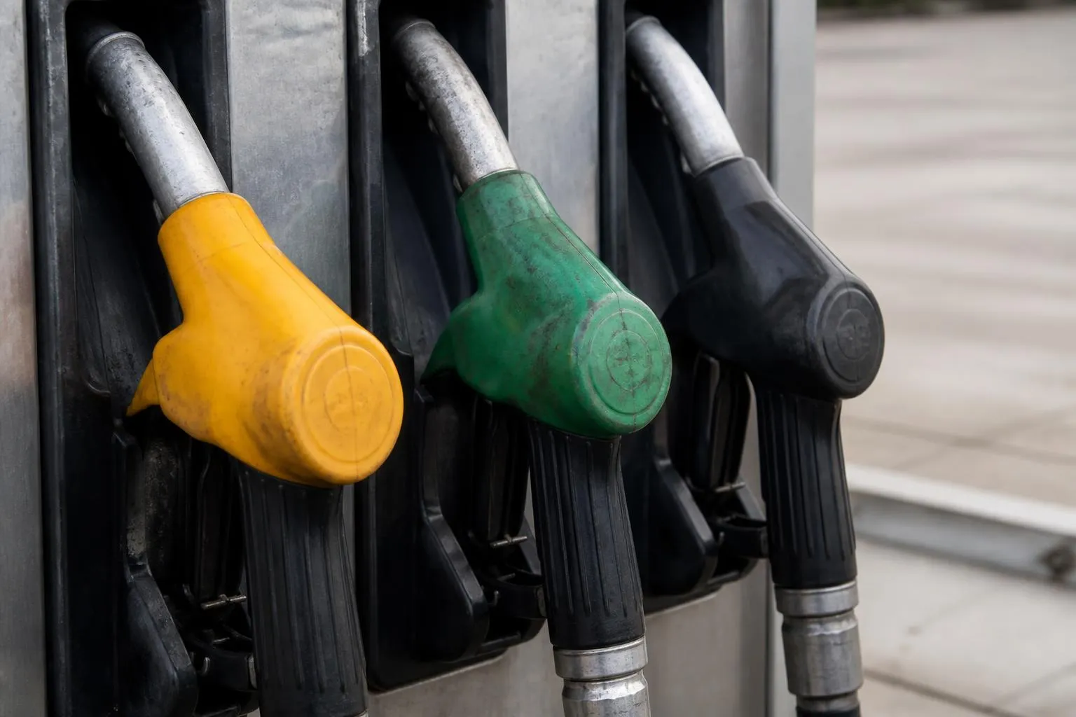 Trois pistolets de distribution alignés sur une pompe à carburant, poignées usées.