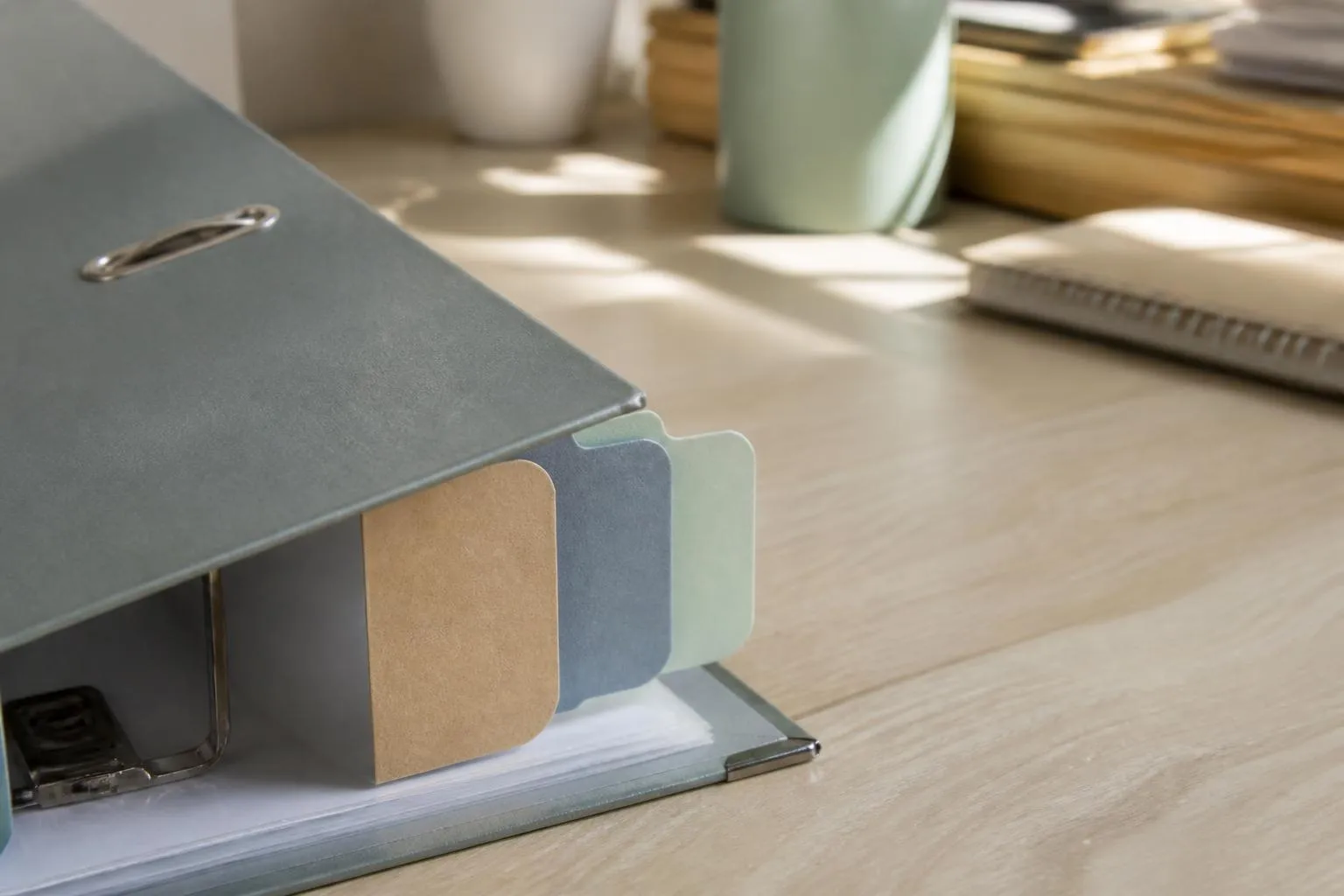 Trois intercalaires cartonnés de couleurs différentes dépassant d’un classeur ouvert posé sur un bureau en bois